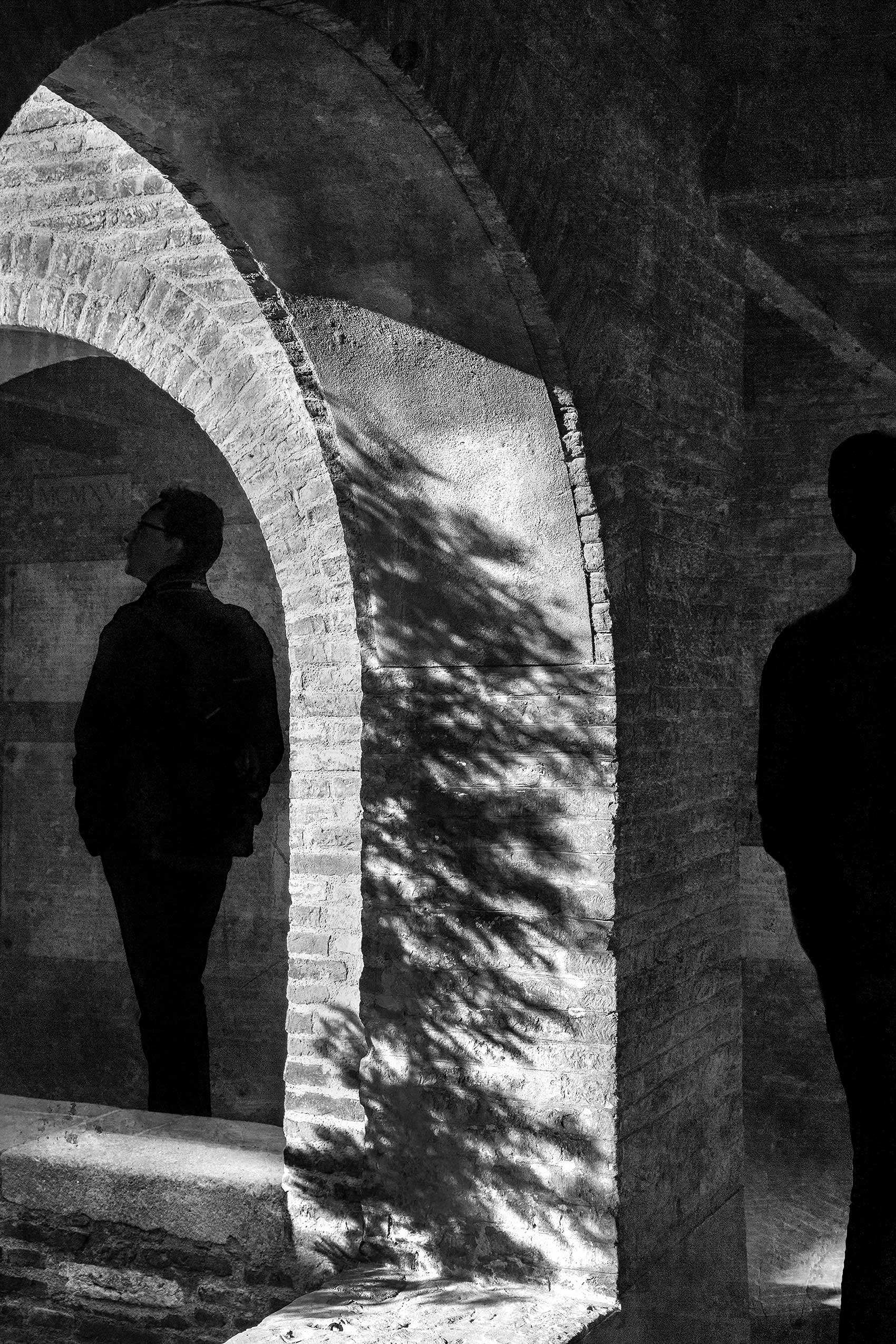 Visitors walking under the porticoes of the 11th century Cloister of the Celestines. Cloister Shadows