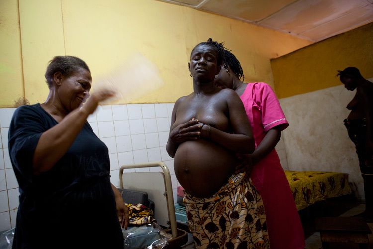 Mother-to-be Aisatu Kabu, 35yrs in labour with her 5th child at Kroo Bay Community Health Centre, Freetown, Sierra Leone. Aisatu is attended to by both a Traditional Birthing Attendant (TBA) Tenneh Oldfield and A trained Maternal and Child Health Aid (MCHA, midwife) Adama T. Bangura. There is just one labour room at the clinic and Aisatu has her son whilst another woman on the next bed also prepares to give birth. Commissioned for VSO. 1sierra_leone_childbirth.jpg
