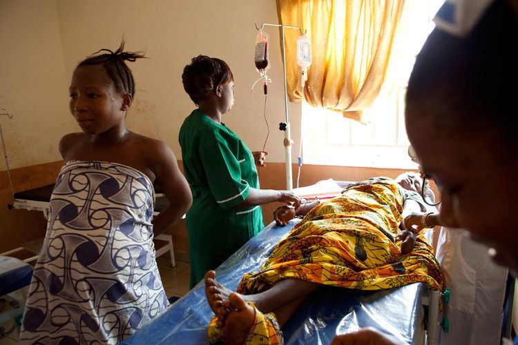 The labour room, Makeni Government Hospital. Up to five women may be in labour at one time in this room. There are no pain relieving drugs available. Inducement is done using a catheter. It is very common for new mothers to experience complications in childbirth due to a number of factors including obstructed birth canal from Female Genital Mutilation, FGM (estimated 90% of female population has had FGM) Haemorraging, anaemia, eclampsia and the need for emergency blood transfusion. Maternal death rates are high, 857 per 100,000. One of the worst in the world. Child mortality is the worst in the world. 1 in 4 children below the age of 5 die each year. Makeni, Sierra Leone. 1sierra_leone_women_birth_7.jpg