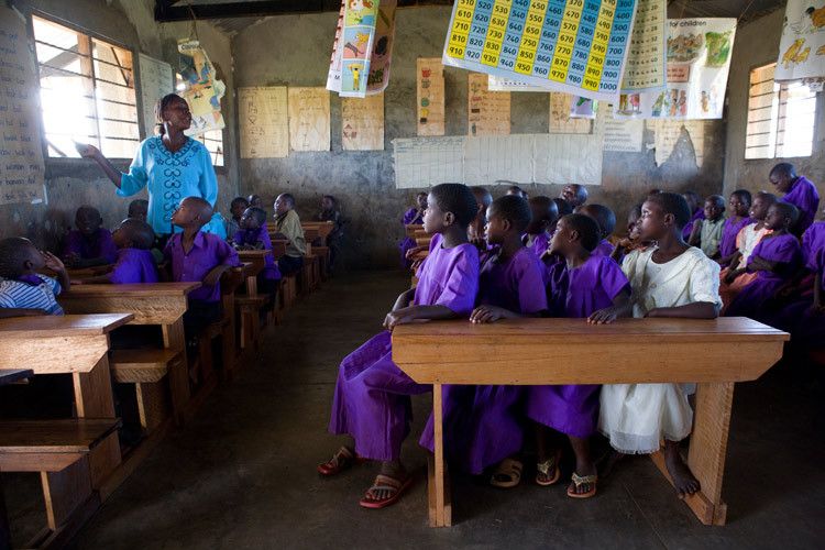 Teenage girls squeeze onto a bench during lessons at Kitemba primary school. Girls often miss weeks at a time of their education due to parents taking them out of school to help with farming. Boys' education is prioritised and their studies usually remain uninterrupted . This can result in 17 year old females repeatedly trying to pass end of year exams in order to progress to secondary school. Mubende, Uganda for ActionAid. 1uganda_education_14.jpg