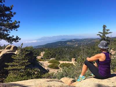 A girl sitting on a rock overlooking forested mountain view