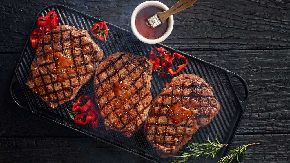 Three steaks on cast iron crill with hot peppers