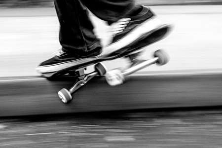 Mikkel Bang. Burlington, VT flies along a curb grinding high speed with motion blur in black and white Skateboarder grinds curb going fast