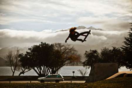 Shaun White. Wanaka, New Zealand grabbing his skateboard flying through the air with hair. Shaun White flies through air on skateboard in front of mountains