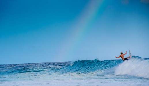 John John Florence. North Shore, Oahu Hawaii slashes waves on a surfboard under a rainbow in the morning Surfer turns on a wave under a rainbow