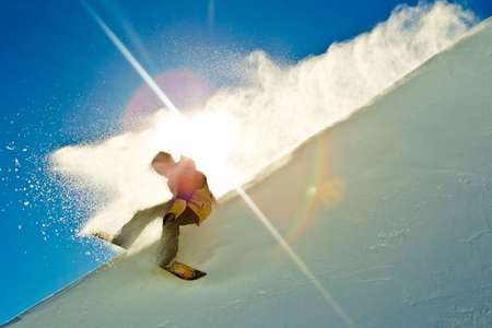 Christian Haller.Snowpark, NZ shreds the lip in a burst of sunshine exploding snow in the air Snowboarder slides down halfpipe through the sun