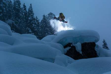 Mikkel Bang. Whistler, BC in evening backlit flash powered light. Grabbing his snowboard with amazing style A snowboarder flies above a field of backcountry powder pillows