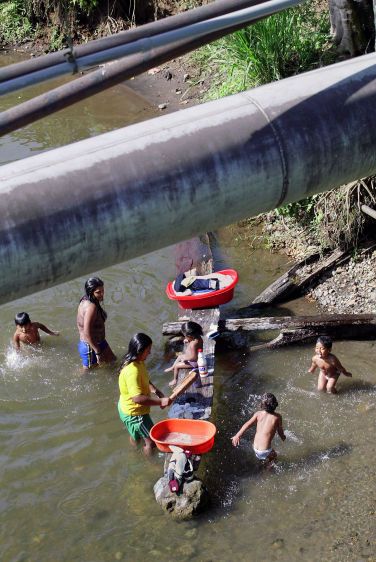 A family washes clothes and bathes under an oil pipeline in a polluted river near Lago Agrio.