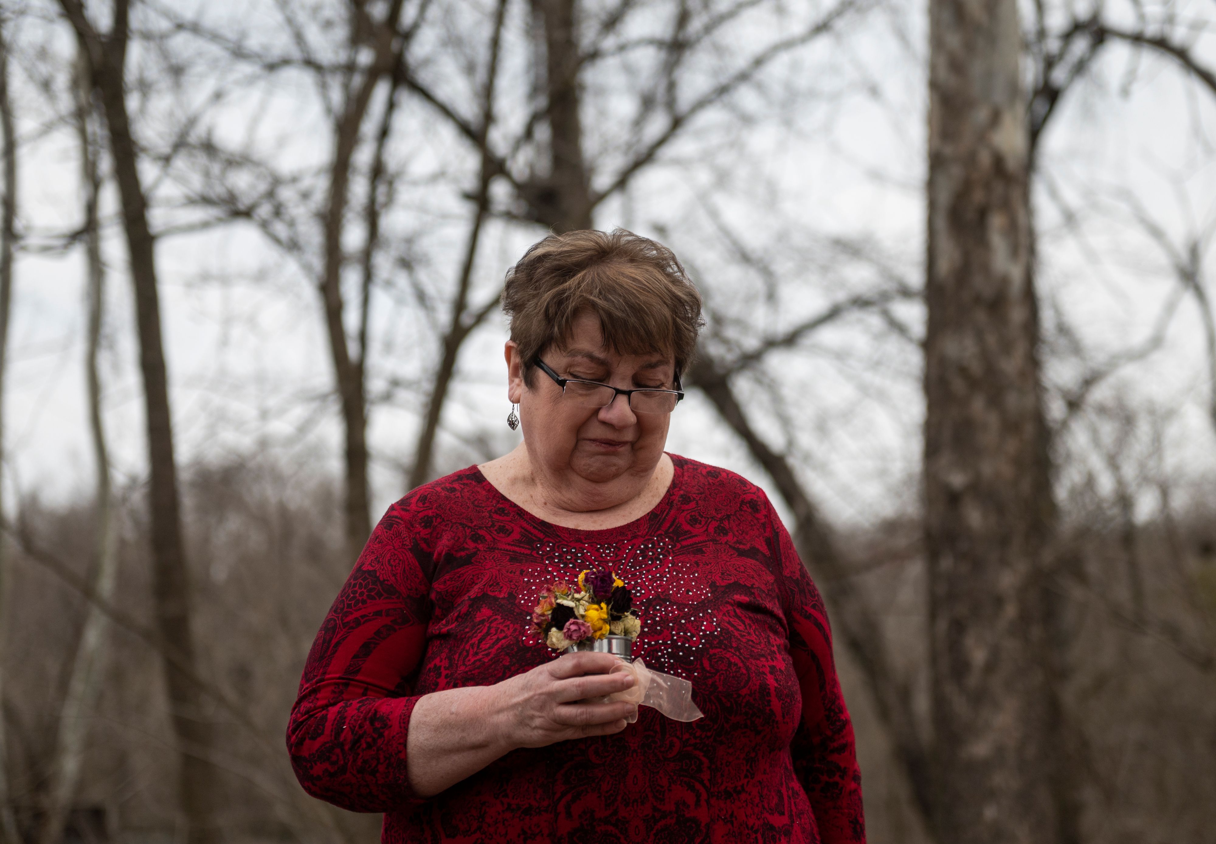 Sue Irvine cries as she holds flowers given to her by Jan Trent in memory of her son Chris Irvine, who passed from Covid-19 in January, near the James river in Lynchburg 94X76M.jpg