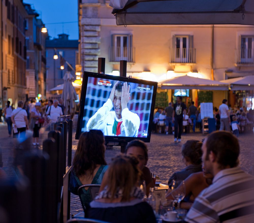 Televised italian World Cup at outdoor restaurant on square.