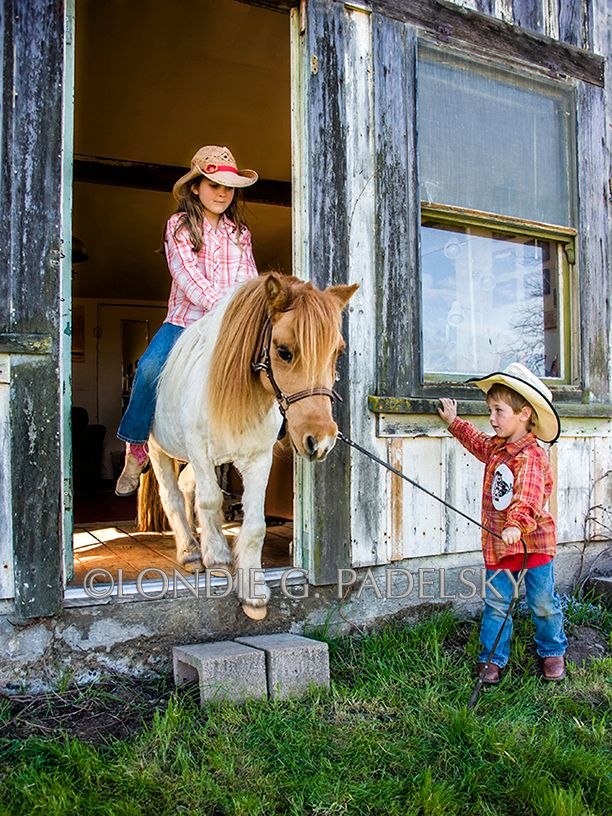 Little cowboy leads pony out the old cabin door while a little cowgirl rides on top.                                 ©Londie G. Padelsky SLO_LGP5447_LondieGPadelsky