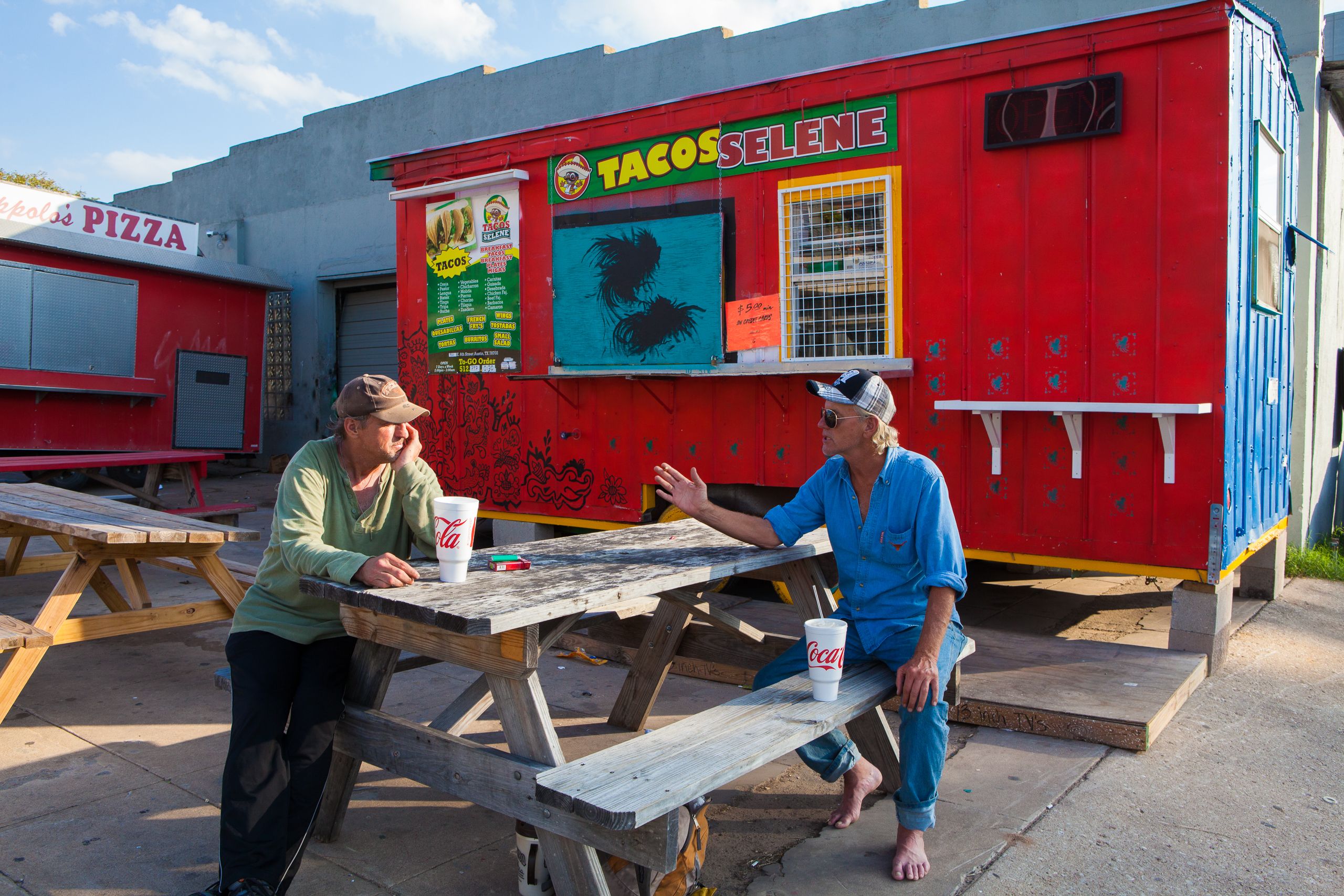 Two homeless men argue in front of a taco stand.