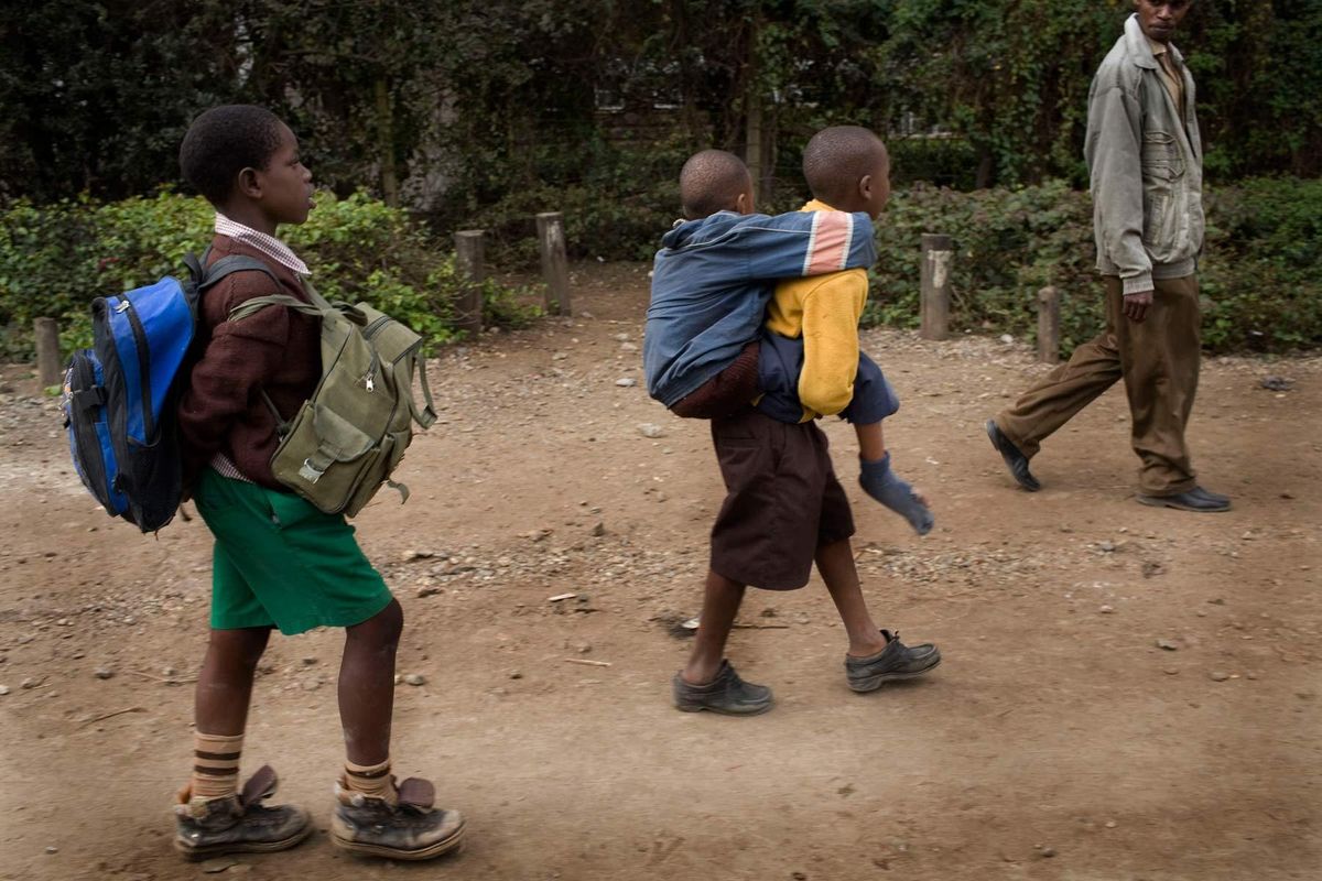 Mutava carrying Braise back from School to home. On the way home another friend and neighbour always routinely carries their bags for them, as Mutava is unable to carry both Braise and the bags.© Hazel Thompson Carried on friendship