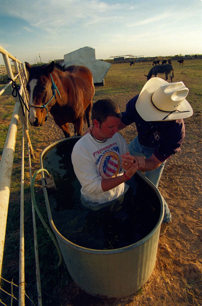 Baptism Cowboy style! - Pastor Monty Price baptises Shaun by full immersion in his horses' drinking trough.© Hazel Thompson Modern Crusaders