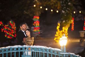 Romantic, Christmas-Lighted Embrace on Snow-Covered Bridge Bride and Groom