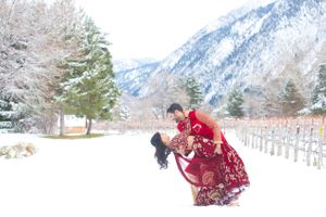 Striking Red-Costumed Indian Bride Being Dipped in Front of Snow-Covered Mountains Pre-Ceremony