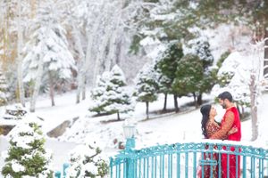 Brilliant, Red-Costumed Indian Couple Embraces on Pale-Blue, Snow-Covered Bridge Pre-Ceremony