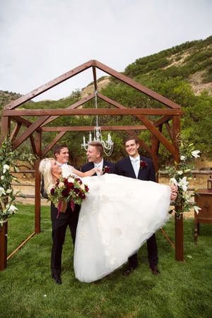 Hoopes Events | Tori and Sterling | Quiet Meadow Farms | Mapleton Utah | Bride Laying on Groom and Groomsmen's Arms in Front of Chandelier Backdrop Tori_Sterling_Quiet_Meadow_Farms_Mapleton_Utah_Bride_Laying_on_Groom_Groomsmens_Arms.jpg