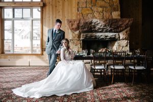 Hoopes Events | Rocky Mountain Bride | Winter Elopement | Deer Valley | Empire Lodge | Park City Utah | Bride Seated at Table With Groom Standing Beside Her Rocky_Mountain_Bride_Winter_Elopement_Deer_Valley_Empire_Lodge_Deer_Valley_Resort_Park_City_Utah_Bride_Groom_Seated_Table.jpg