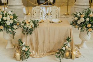 Sweetheart table with large floral arrangements and a gold sequin table cloth. Ceremony